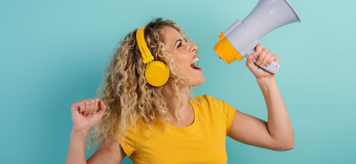 Woman sings with loudspeaker and listen to music with headset. joyful expression. cyan background